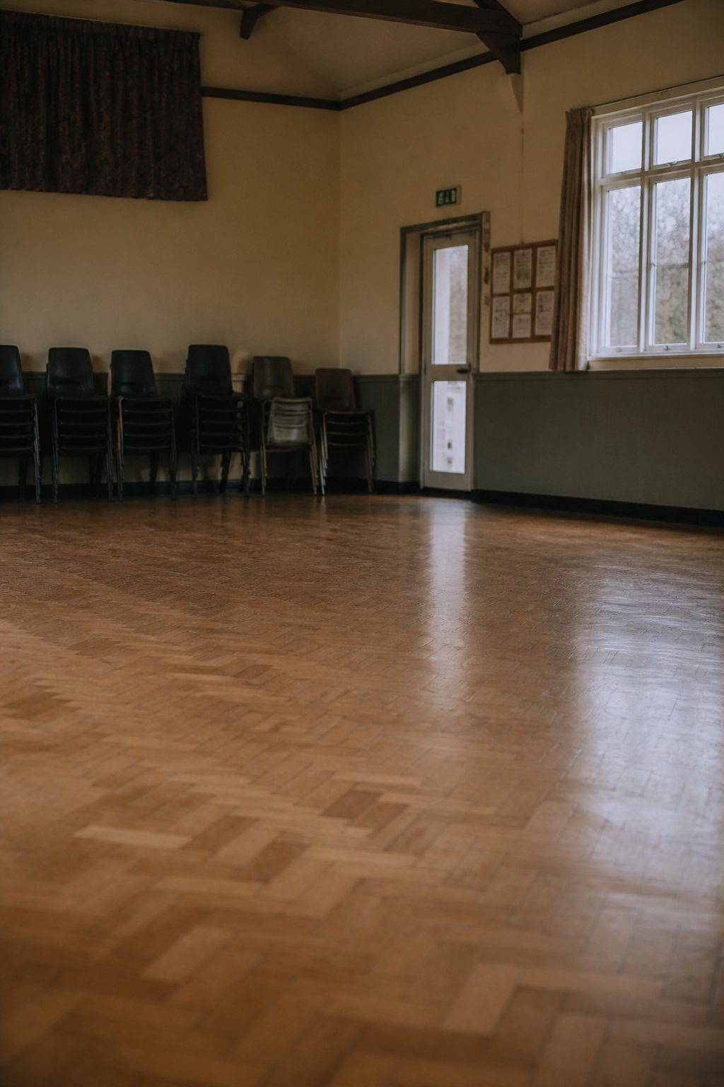 A printed Lutheran hymnal open on a wooden pew ledge in an empty nave, late morning light falling across the page from a clear window, shot from just above...
